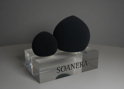 Two black beauty sponges on a clear stand with 'SOANERA' branding against a gray background.