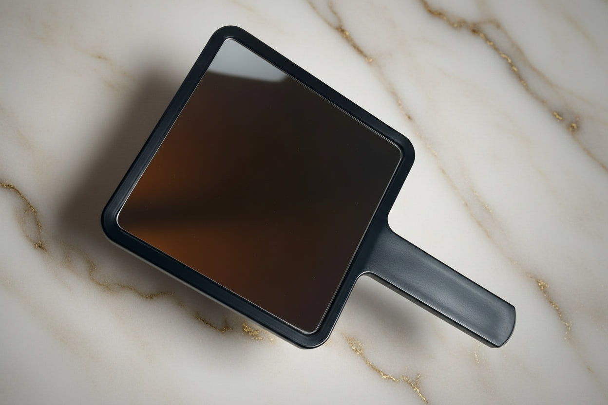 Handheld mirror with black frame on a beige marble background