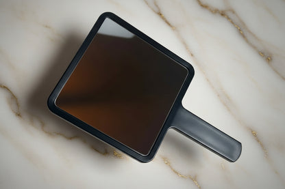 Handheld mirror with black frame on a beige marble background