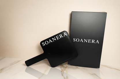 Black handheld mirror and packaging with 'SOANERA' branding on a beige and marble background